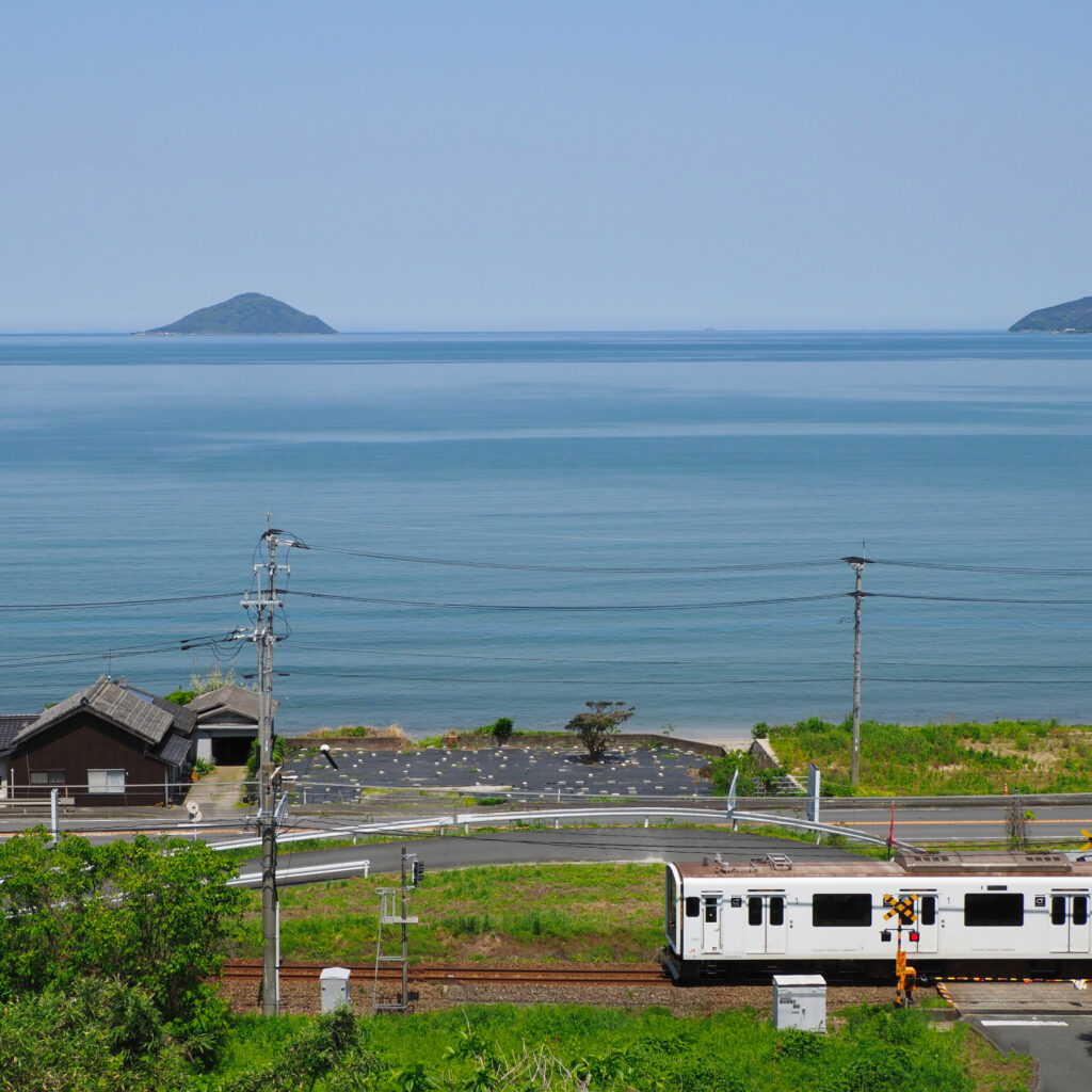 二丈福井の高台から撮影した白い電車と広がる青い海、遠くの島々が浮かぶ絶景構図